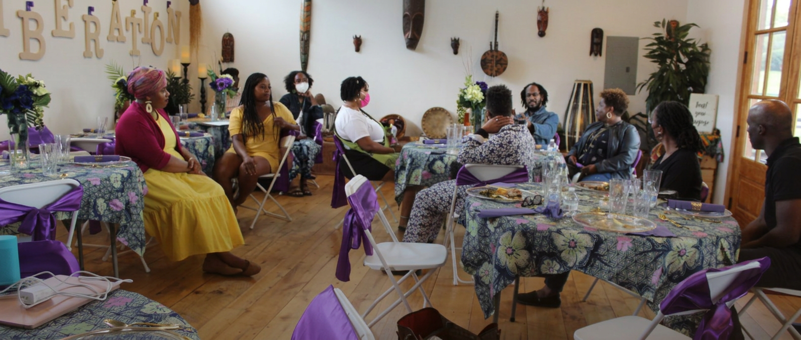 Neighbors seated together at round dinner tables with purple linens, beneath wooden letters spelling LIBERATION